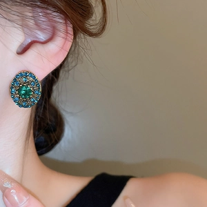 Close-up of vintage oval earring with blue crystals and a green gemstone on ear