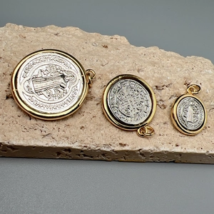 Three gold-framed Saint Benedict cross pendants in various sizes on a natural stone surface