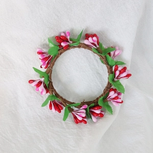 Close-up of pink berry candle ring with green leaves on textured linen background