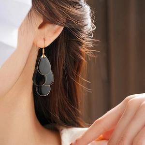 Macro shot of tiered black enamel water drop earrings on a model with golden hooks