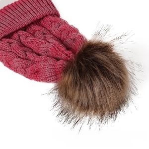 Detailed view of magenta winter beanie featuring thick cable knit and a brown faux fur pom