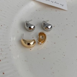 Detailed top view of gold and silver bean-shaped C-style stud earrings on white ceramic tray