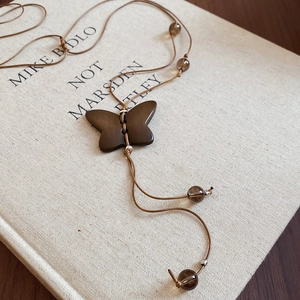 Macro d'un pendentif papillon en bois sur un long collier tissé avec des perles marrons