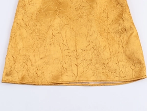 Detailopname van de gouden satijnen stoftextuur en geplooide zoom van deze jurk