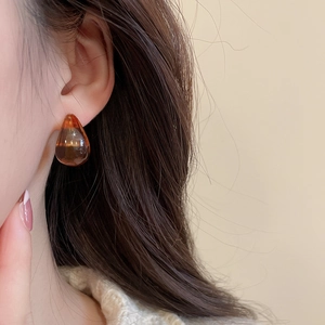 Close-up of elegant amber acrylic teardrop earrings worn on ear with minimalist style