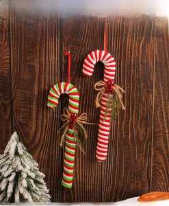 Detail of plush candy cane ornaments with bows, bells, and pine leaves on dark wood