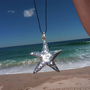 Y2K vintage silver starfish pendant with black cord on beach background