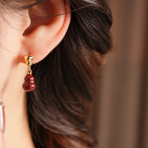 Close-up of 18k gold plated earrings with wine red gourd pendant on a model's ear