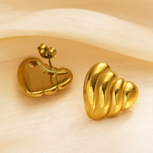 Gros plan de boucles d'oreilles cœur dorées avec texture ondulée 3D sur soie beige