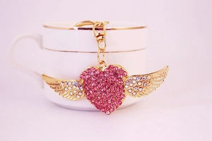 Close-up of golden heart keychain with pink rhinestones and angel wings detail