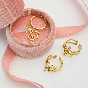 Three elegant gold musical note rings displayed on pink velvet boxes for gift sets