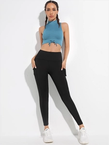 Dettaglio di leggings yoga a vita alta con tasche laterali e crop top blu con lacci incrociati