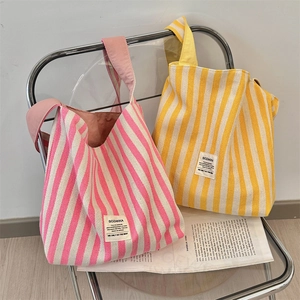 Dettaglio di borse tote in tela a righe rosa e gialle con etichetta minimalista del brand