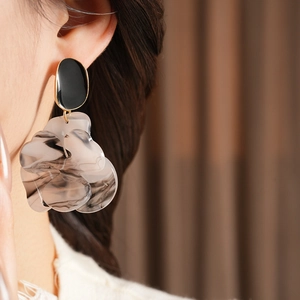 Close-up of marble-textured resin flower earrings with gold edges worn by a model