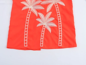 Detailed view of white palm tree embroidery on a vibrant orange summer vacation dress