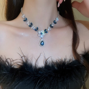 Close-up of a silver necklace with dark blue zircons and teardrop pendant on a model
