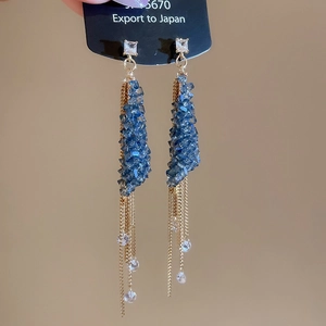 Close-up of elegant gold tassel earrings with blue crystals and hanging fine chains