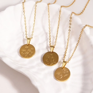 Detailed view of three gold titanium necklaces with engraved floral patterns on a shell tray