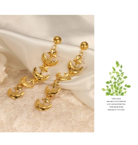 Macro detail of gold-plated celestial earrings featuring star, moon, and floral engraving