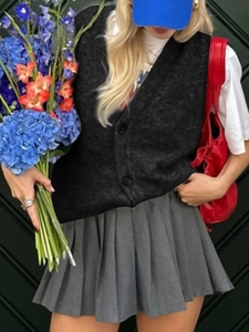 Dettaglio di un gilet in maglia nera con scollo a V e una gonna a pieghe grigia all'aperto