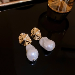 Detail of star-shaped gold metal earrings with large baroque white pearl drops on black surface
