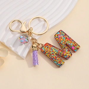 Detail of glitter letter M resin keychain with purple tassel and star filled ball charms