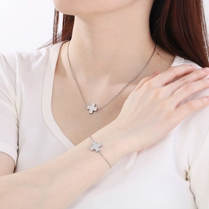 Close-up of a silver cross pendant necklace and matching slim bracelet set on a model