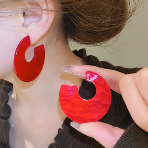Macro detail of red acrylic C-shaped earrings with marble texture on earlobe