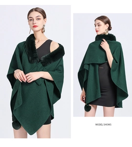 Close-up detail of dark green knit cape with thick faux rabbit fur collar and soft pom-pom trim