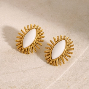 Macro shot of gold sunburst earrings with white eye-shaped enamel inlay on stone