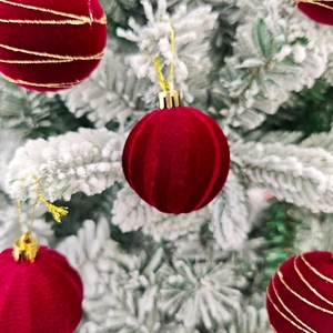 Détail de boules de Noël en velours rouge avec rayures dorées sur branches enneigées