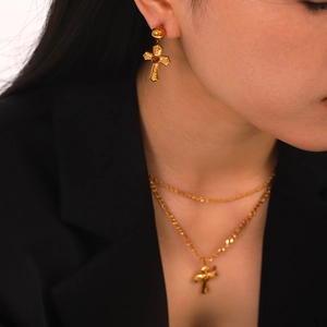 Detail of model wearing a gold cross pendant necklace and matching textured earrings
