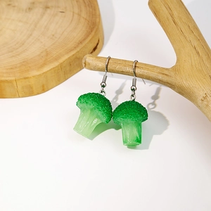 Detailed view of realistic broccoli-shaped resin earrings hanging on a natural wood branch