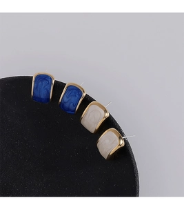 Detailed close-up of blue and off-white enamel stud earrings on a black matte display stand