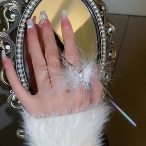 Detail view of a feather butterfly ring with rhinestones worn on finger near vintage mirror