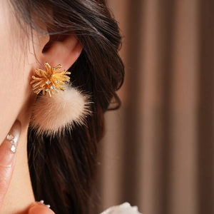 Close-up of golden firework stud earring with clear crystals and a beige faux fur pompom