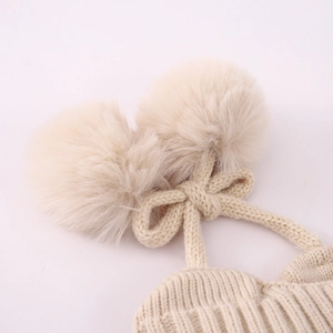 Detalle del gorro de punto cálido con dos pompones de felpa y un adorno de lazo suave