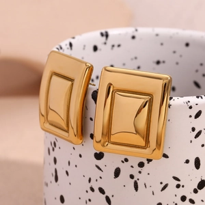 Macro shot of geometric rectangular 18K gold-plated earrings on artistic ceramic cup