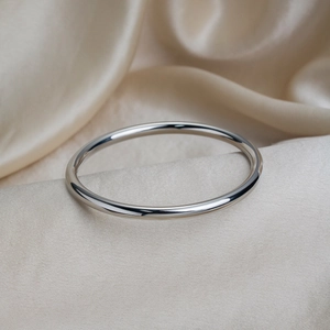 Polished silver minimalist hollow bangle resting on soft white satin fabric background