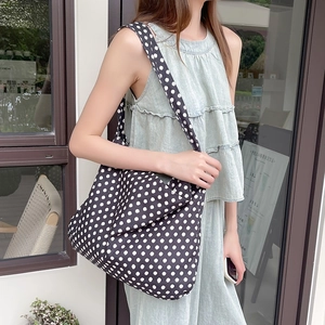 Close-up of black and white polka dot canvas tote bag worn by a model in a casual setting