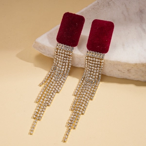 Détail de boucles d'oreilles en velours rouge avec pompons dorés et strass brillants