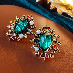 Detailed close-up of emerald green vintage earrings with pearls and gold floral metal frame