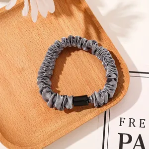 Close-up of a grey satin scrunchie with pleated texture on a wooden tray with flowers