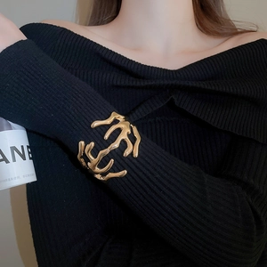 Detail of artistic gold branch open cuff bracelet over a black knit sleeve