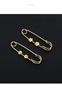 Detail of golden safety pin clips with floral and geometric charms on black background