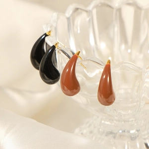 Elegant enamel teardrop earrings in black and brown hanging on a vintage glass cup