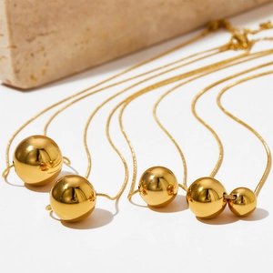 Polished gold hollow sphere pendant necklaces with sleek snake chains on a stone backdrop