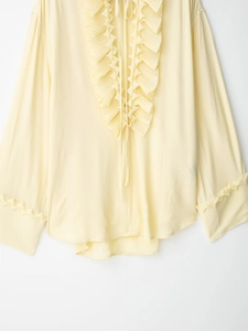 Detail of light yellow ruffle neck blouse featuring textured fabric and ruffled cuffs