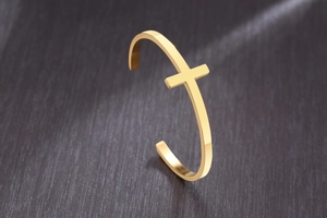 Close-up of polished gold cuff bracelet featuring a minimalist cross design and mirror finish