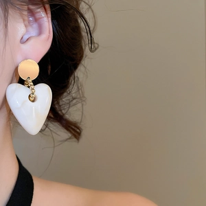 Close-up of elegant white acrylic heart earrings with gold studs worn by a model